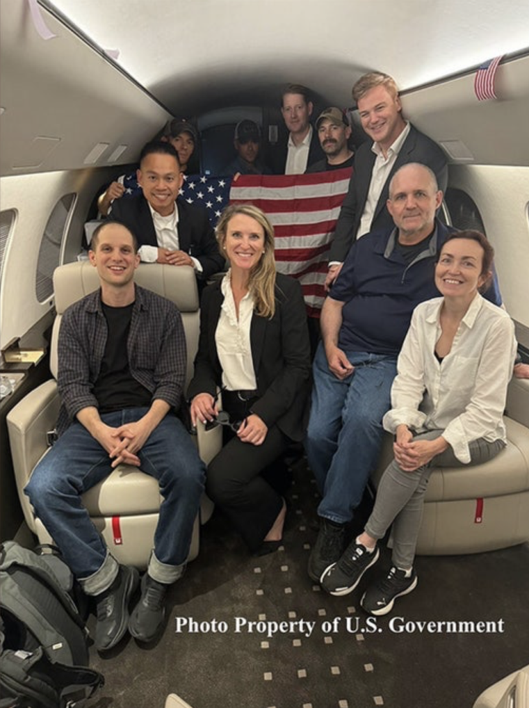 Evan Gershkovich, Alsu Kurmasheva, and Paul Whelan smile aboard an airplane after being released from Russian prison in a historic prisioner swap on Thursday, August 1, 2024. (U.S. Government)